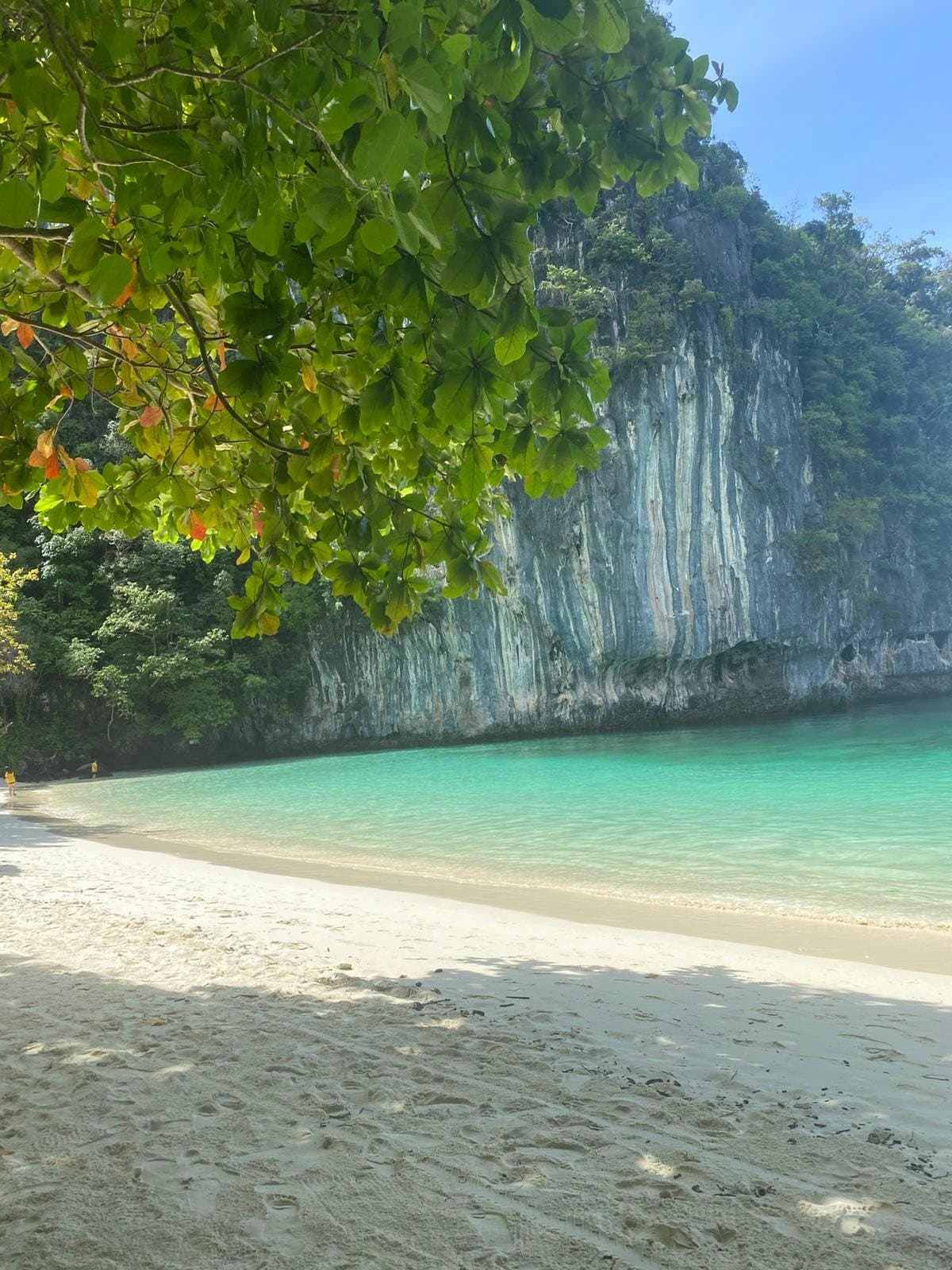 The curve of Hong beach, white sand and pale green water below a streaked limestone cliff