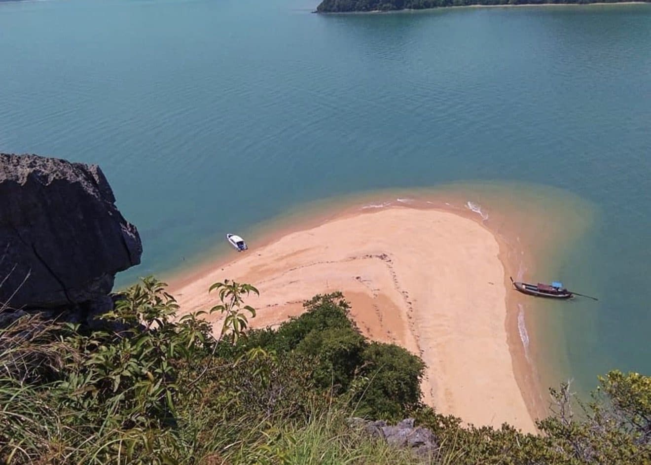 A curved sand spit at Koh Nok from above, a longtail and a speedboat moored in shallow green water