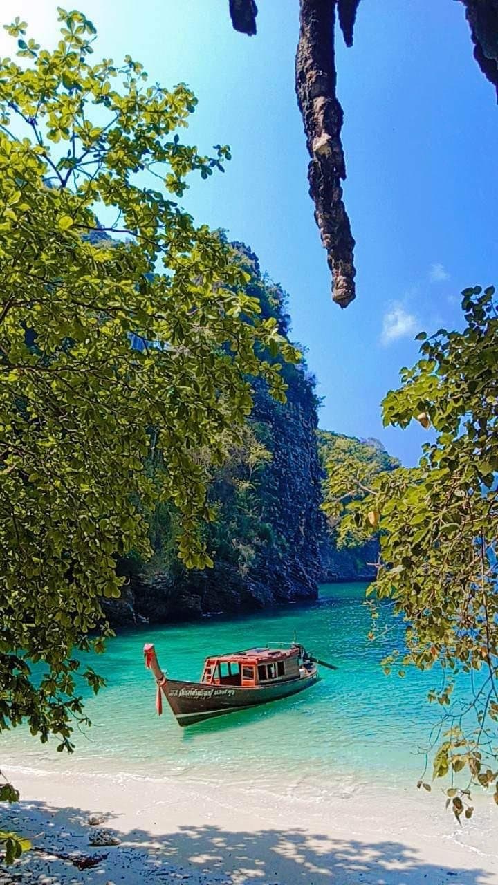 A longtail boat on clear turquoise water in a sheltered bay behind Koh Poda, framed by overhanging branches